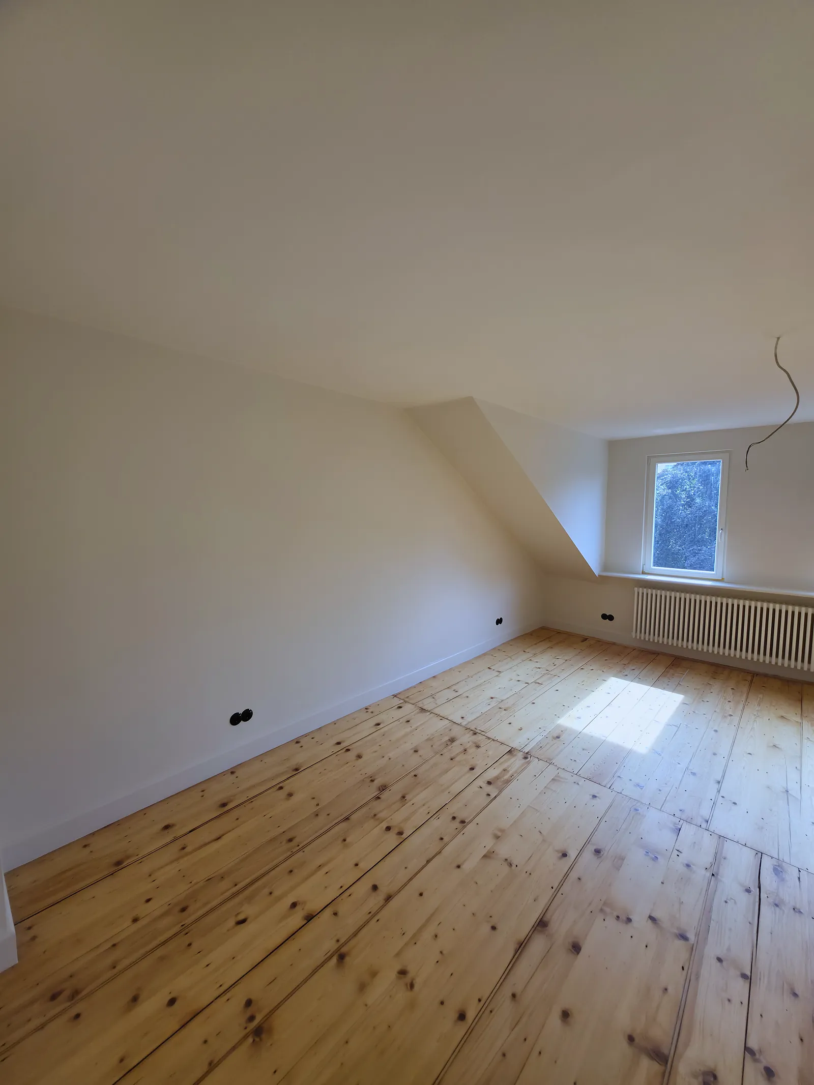 Poddasze z gładką ścianą i skosem, okno i kaloryfer pod nim